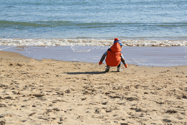 Niño está buscando piedras en la playa
 - Foto, imagen