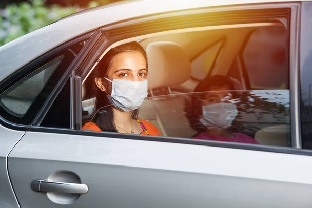 Індійська дочка, одягнена в маску обличчя або медичну маску під час водіння автомобіля. - Фото, зображення