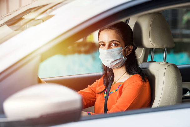 Hermosa joven india en una máscara sentada en un coche, máscara protectora contra el coronavirus, conductor en una calle de la ciudad durante la pandemia covid-19
 - Foto, imagen