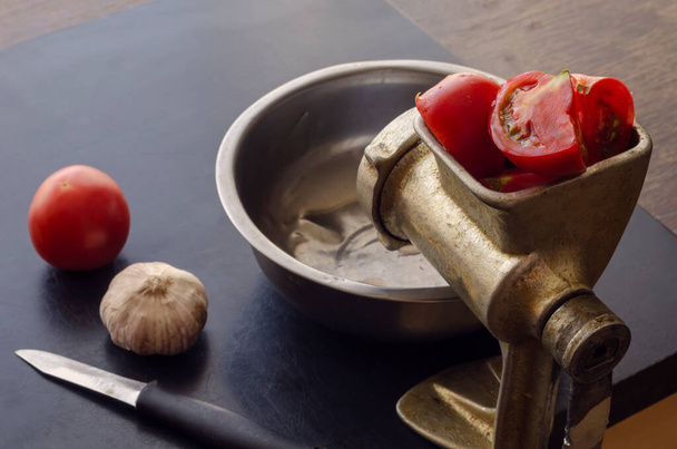 Broyeur manuel de viande vintage, couteau et légumes sur la table. Tomates mûres et une tête d'ail. Utilisation d'ustensiles de cuisine obsolètes. - Photo, image