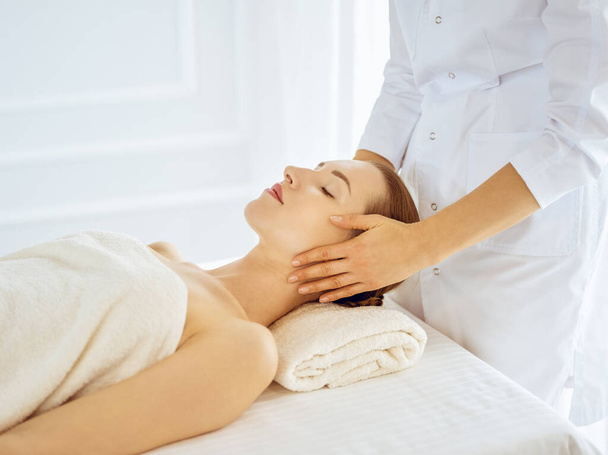 Beautiful woman enjoying facial massage with closed eyes. Spa treatment concept in medicine - Фото, изображение