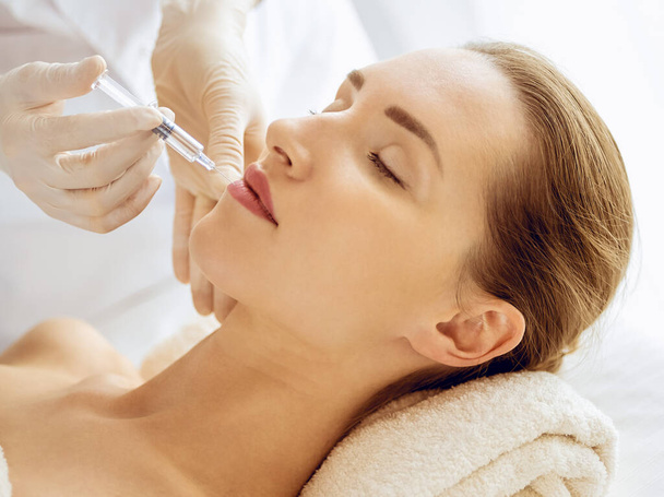 Beautiful woman receiving beauty injections with closed eyes. Beautician doctor hands doing beauty procedure to female face with syringe. Cosmetic medicine and surgery concept - Photo, image