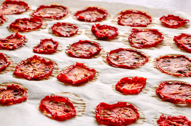 Kawałki suszonych pomidorów na pergaminie. Zbliżenie porcji przyrządzonych odwodnionych warzyw. Suszone jedzenie. Skupienie selektywne. - Zdjęcie, obraz