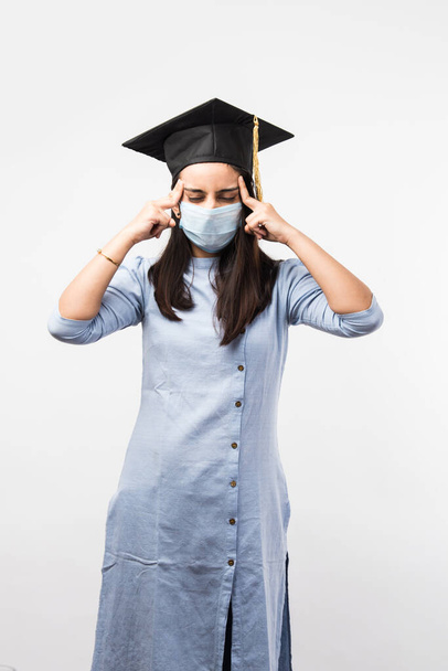 Корона Пандемика и путаница с университетскими экзаменами в Индии - Прекрасная индийская студентка с запутанными выражениями лица в медицинской маске и выпускной шляпе - Фото, изображение