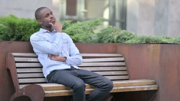 Offensiver junger Afrikaner sitzt auf Bank und denkt nach  - Filmmaterial, Video