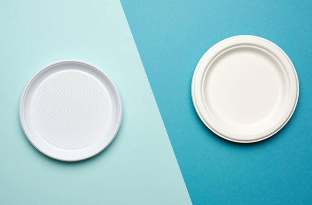 empty white plastic plates and white paper disposable plates on a blue background, top view. The concept of rejection of plastic, environmental conservation - Фото, изображение