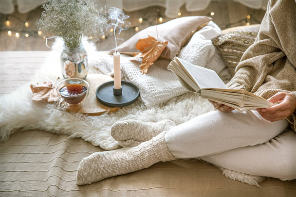 Confortable automne à la maison, une femme avec du thé et un livre de repos. Un mode de vie confortable. Parties du corps dans la composition. - Photo, image