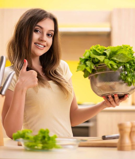 Young woman preparing salad at home in kitchen - Fotó, kép