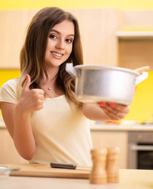 jonge vrouw koken soep in keuken thuis - Foto, afbeelding