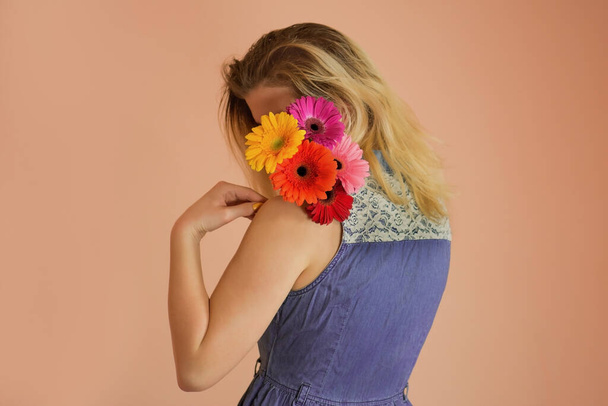 Весела молода леді в джинсовій сукні і квіти ромашки в руках
 - Фото, зображення