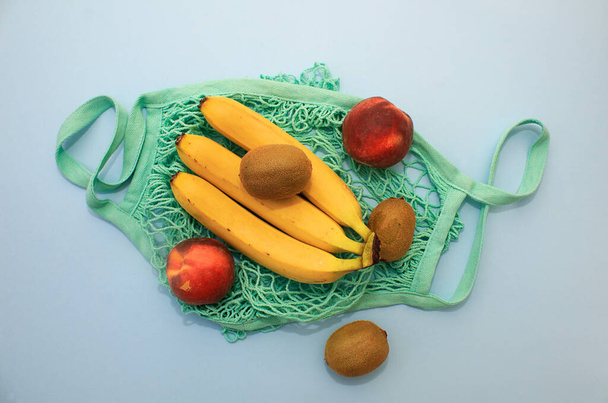 果物キウイ、バナナ、青の背景に桃と綿の緑のストリングバッグ。プラスチックを使わない環境に優しいショッピング - 写真・画像