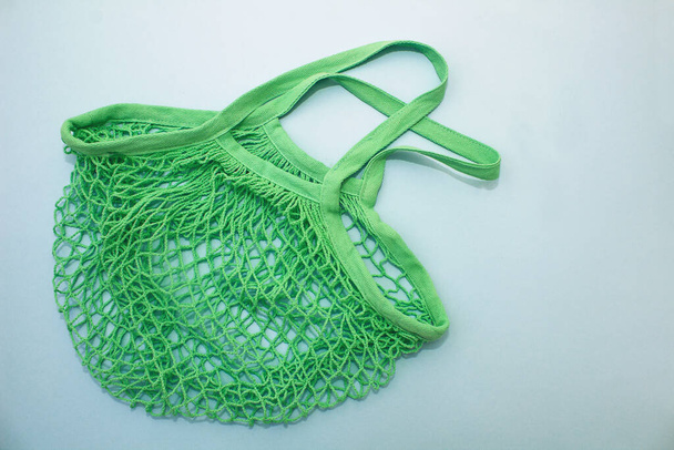 Cotton green mesh bag on blue paper background. Eco-friendly shopping without plastic - Fotó, kép