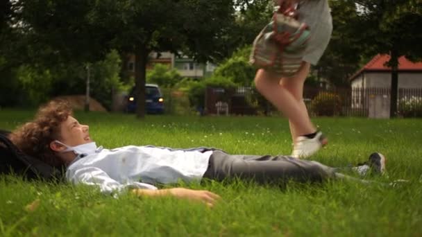 Classmates, boy and girl are resting lying on the grass during school break. Back to school, social distance, contactless greeting - Materiał filmowy, wideo