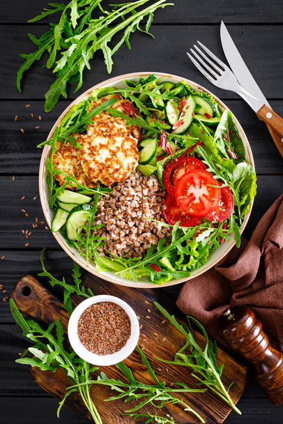 Lunch bowl with buckwheat porridge, fried chicken cutlets and fresh vegetable salad of arugula, lettuce, chard leaves, tomato, cucumber and flax seeds - Fotografie, Obrázek