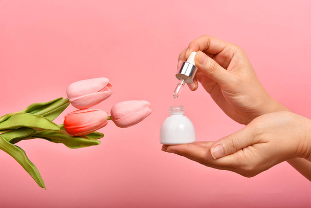 Natürliche Hautpflegeflasche, Hand zeigt fallende Kosmetikbehälter Verpackung mit Tulpenblüten Essenz-Extrakt, Bio-Beauty-Produktkonzept. - Foto, Bild