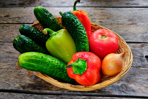 Cucumbers, tomatoes, sweet bell peppers and onions in a basket on a wooden table in a rustic style - Фото, изображение