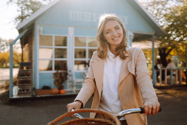 Beautiful girl with a bike on the background of a blue house in the fall. - Fotó, kép