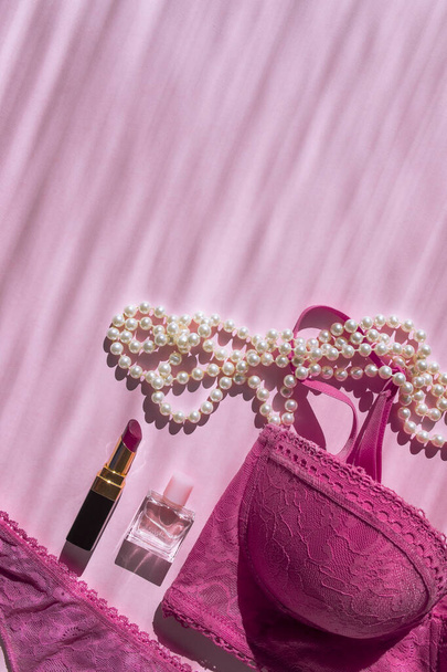 Lingerie bra and panties, perfume bottle, lipstick and pearl beads. Pink flatlay top view with place for text. Picture with sunbeams. Taking care of yourself. Self-love. Fashionable modern girl stuff - Foto, Bild
