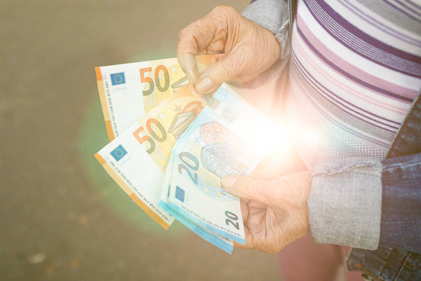 Handen van een oudere vrouw met eurobankbiljetten in het zonlicht. Begrip welvaart, ouderdom veiligstellen, de loterij winnen. Selectieve focus. - Foto, afbeelding