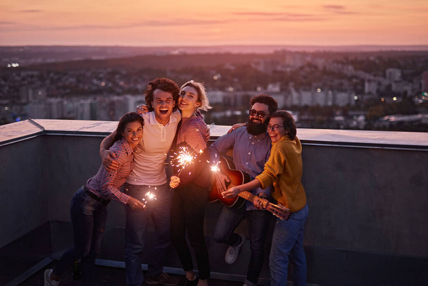 Happy friends with sparklers on rooftop in evening - Foto, immagini