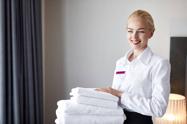 good-looking chambermaid with white linen and towels in her hands - Фото, изображение