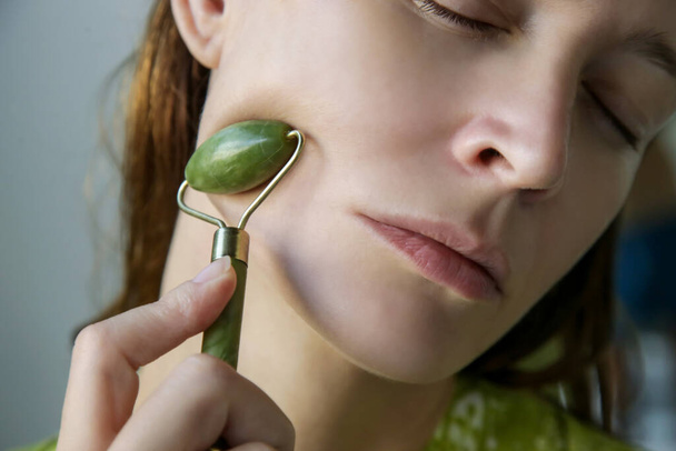 Face massage. Woman using jade face roller for skin care. - Foto, imagen