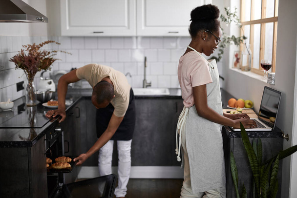 black man takes out baked goods from oven, looks whether it is ready or not - Foto, afbeelding