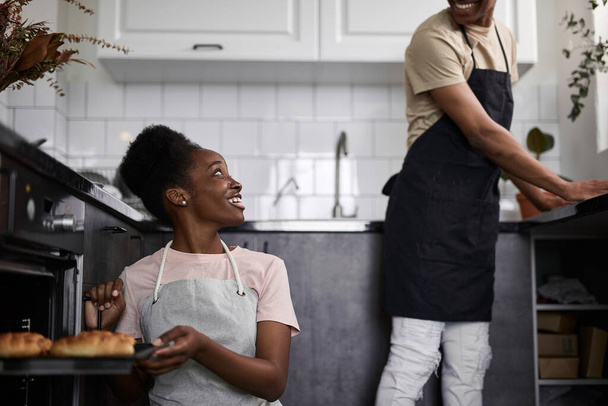 Schwarzes Weibchen öffnet den Ofen, holt gebackene Croissants heraus - Foto, Bild
