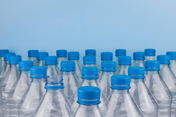 Horizontal color image with a front view of an empty clear plastic bottles with caps stacked on a blue background. Recycling and environment concept. - Foto, Imagem