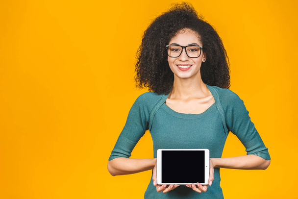 Lächelnde afroamerikanische junge Studentin zeigt leeren Tablet-Computer isoliert auf gelbem Hintergrund. - Foto, Bild