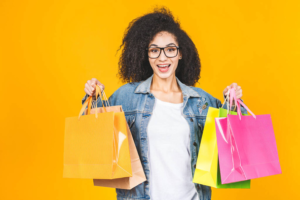 Alışveriş Konsepti - Portre güzel Afro-Amerikan kadın gülümseyen ve renkli alışveriş torbalarıyla dolu sarı Pastel duvar arkasında izole edilmiş. Boşluğu Kopyala. - Fotoğraf, Görsel