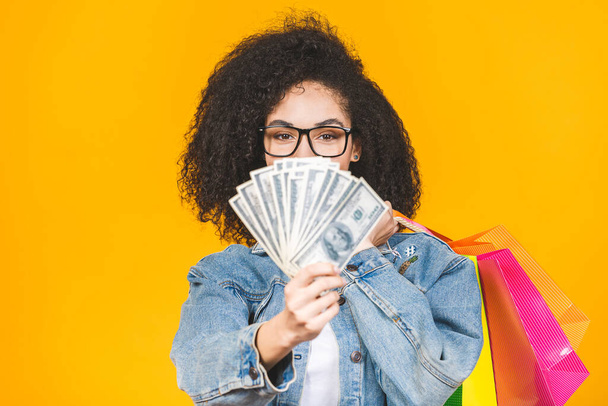 Shopping Concept - Portré fiatal szép afro-amerikai nő mosolyog és örömteli színes bevásárló táskák és a pénz elszigetelt sárga háttér. Fénymásolási tér. - Fotó, kép