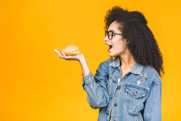 Afroamerikanisch schwarze junge Frau isst Hamburger isoliert auf gelbem Hintergrund. - Foto, Bild