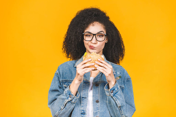 Afrikai amerikai fekete fiatal nő eszik hamburger elszigetelt sárga alapon. - Fotó, kép