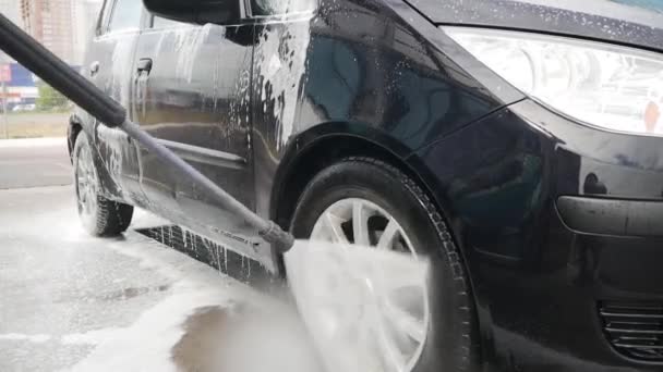 Mies huuhtelee auton suihkuvedellä ja korkeapaineisella vaahdolla itsepalvelupesussa.  - Materiaali, video