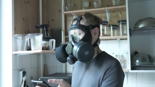 ερεθισμένος άνθρωπος με μάσκα αερίου μιλάει smartphone στην κουζίνα στο σπίτι. προστασία από ιούς - Πλάνα, βίντεο