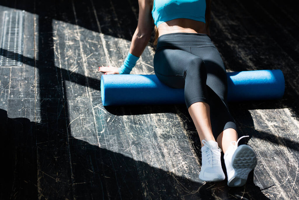 The torso and legs of a slender young woman who goes in for sports in the bright rays of the sun. Working out the fascia of the gluteal muscles with a foam roller - Foto, Bild