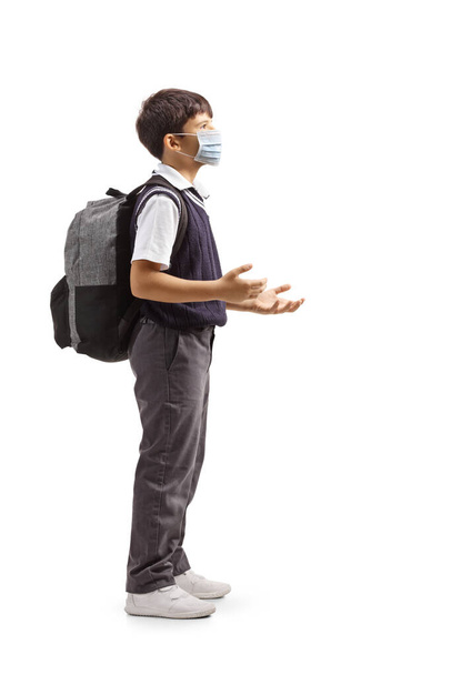 Full length profile shot of a schoolboy talking and wearing a protective face mask isolated on white background - Fotografie, Obrázek