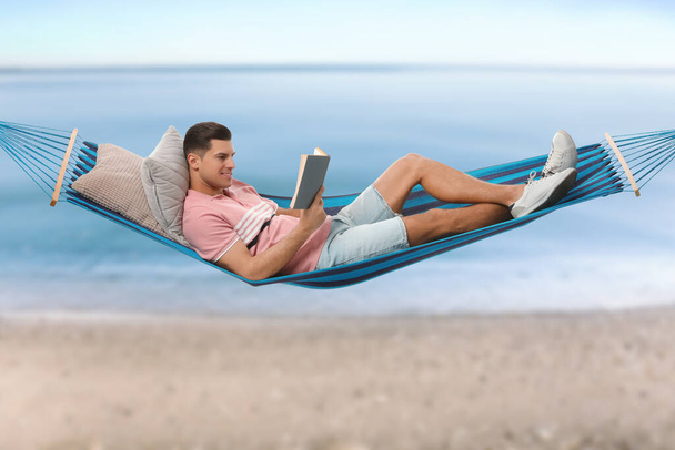 Man reading book in hammock near sea on sunny day  - Фото, изображение