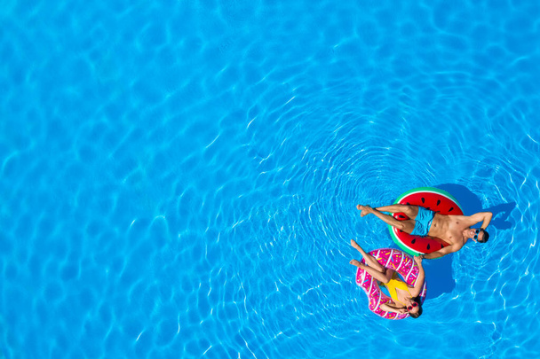 Happy couple with inflatable rings in swimming pool, top view. Space for text  - Fotografie, Obrázek