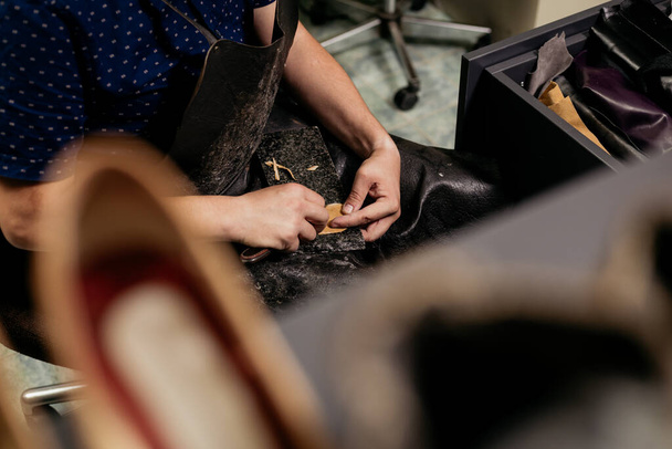 mężczyzna cobler siedzi w jego vintage patrząc warsztat i cięcie skóra tkanina dla buty naprawy - Zdjęcie, obraz