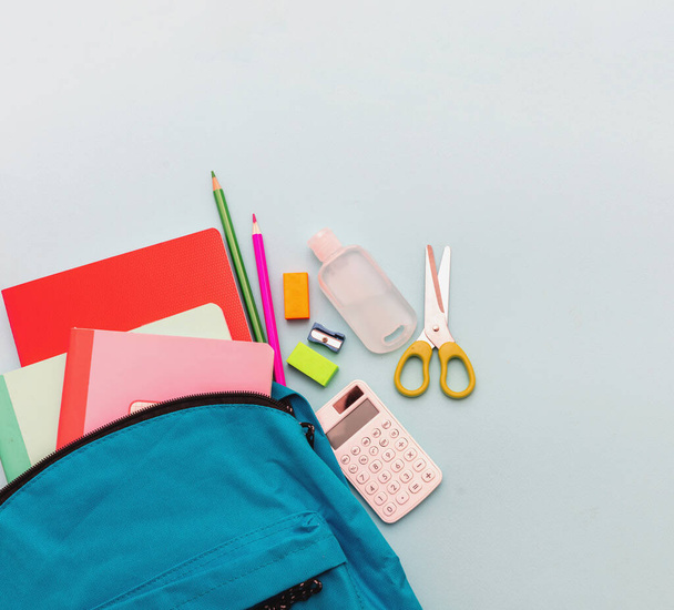 School, coronavirus days. School supplies and sanitizer gel out of a school bag, pastel blue color background, top view, copy spac - Photo, Image