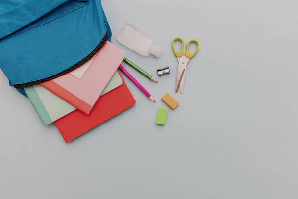 School, coronavirusdagen. Schoolbenodigdheden en ontsmettingsgel uit een schooltas, pastelblauwe achtergrond, bovenaanzicht, kopieerspac - Foto, afbeelding