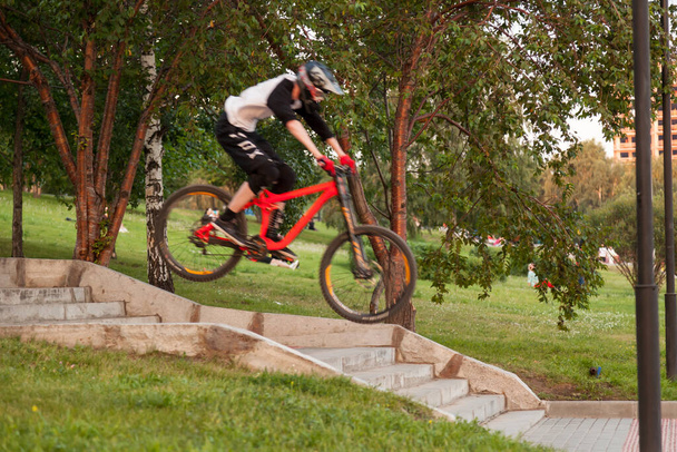 Ένας έφηβος σε ένα ποδήλατο εκτελεί κόλπα πηδώντας πάνω από τις σκάλες κατά τη διάρκεια της κατάρτισης στο πάρκο. - Φωτογραφία, εικόνα
