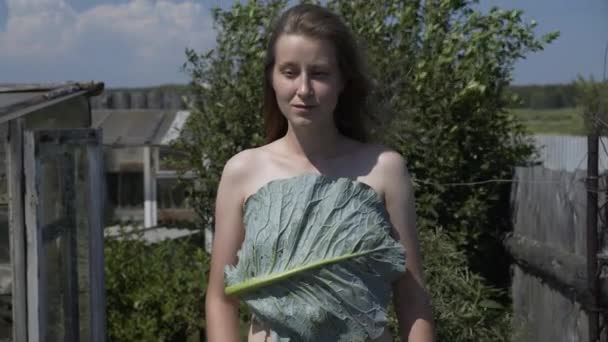 Genç, çıplak bir kadın yaz günü bahçede lahana yaprağının arkasına saklanır. - Video, Çekim
