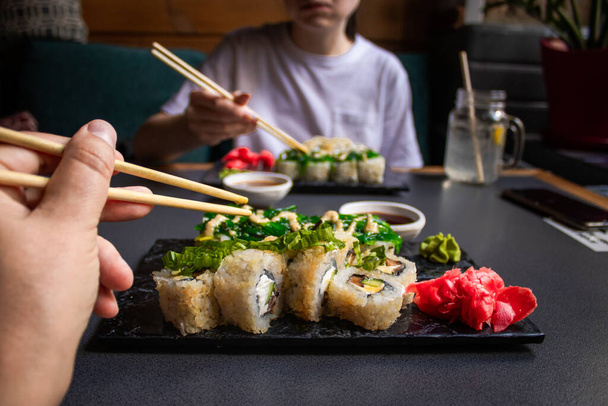 Zbliżenie strony trzymając pałeczki bambusowe z krewetek nigiri podczas moczenia go w sosie sojowym. Szczegóły sushi ustawione na drewnianej tacy w restauracji, podczas gdy ręcznie zanurzyć nigiri w sosie sojowym. Koncepcja kuchni japońskiej. - Zdjęcie, obraz