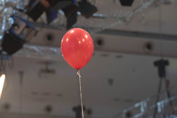 červený balón s připojeným provázkem, rozmazaný strop v pozadí - Fotografie, Obrázek