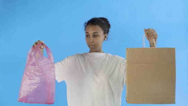 Afro-Amerikaanse Girl Activist maakt een keuze tussen papieren en plastic tas op blauwe achtergrond - Foto, afbeelding
