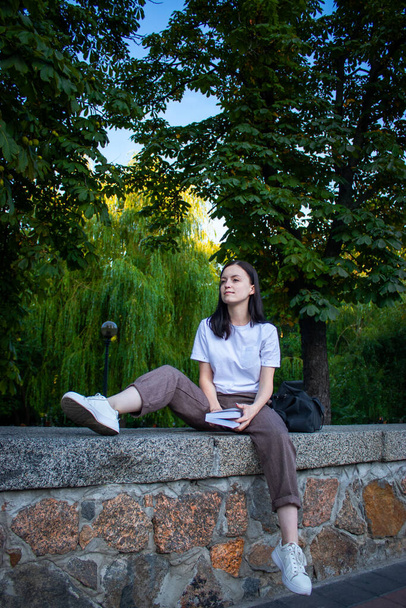 Vista lateral de la mujer morena complacida sentada en el banco y leyendo libro en el parque
 - Foto, imagen