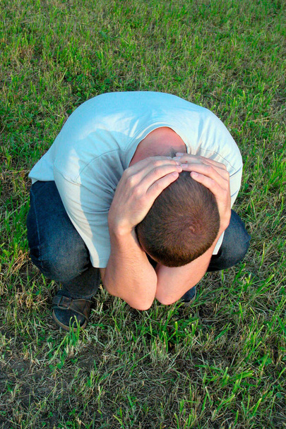 hombre se agacha en un prado verde con las manos en el cuello, símbolo de depresión, salud mental
 - Foto, Imagen